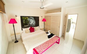 A bedroom with a bed, two bedside lamps, a wall-mounted artwork, a bench, and a wardrobe. - Villas Agua Dulce - Loft Corazon (Sosúa)