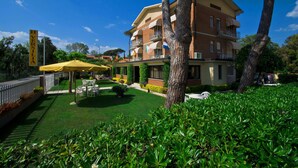 A hotel with a well-maintained garden, outdoor seating, and a prominent 'VERSUS' sign on the building. - Hotel Versilia (Camaiore)