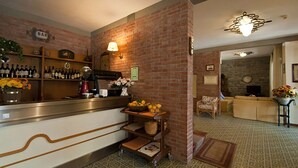 A bar area with a brick wall, shelves of wine bottles, a fruit bowl, and a coffee machine. - Hotel Versilia (Camaiore)