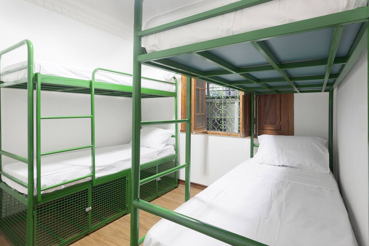 A dormitory room with bunk beds and a window with curtains.