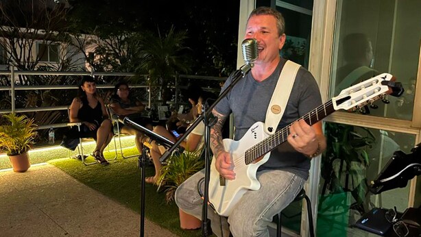 A person playing a white electric guitar and singing into a microphone. - Br Hostel (Belo Horizonte)