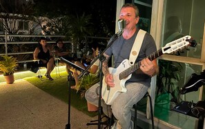 A person playing a white electric guitar and singing into a microphone. - Br Hostel (Belo Horizonte)