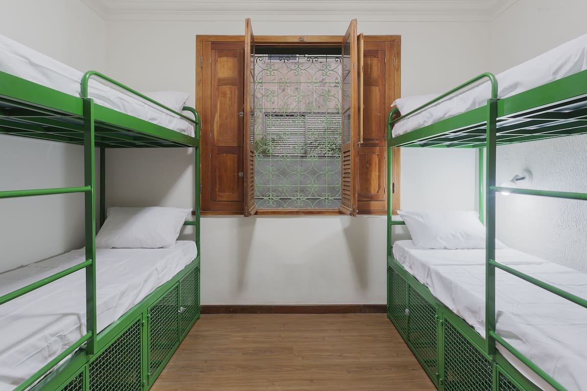 A dormitory room with bunk beds, a wooden window, and a metal grate.