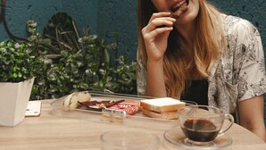 A person sitting at a table with a sandwich, two cups of coffee, and a smartphone. - Br Hostel (Belo Horizonte)