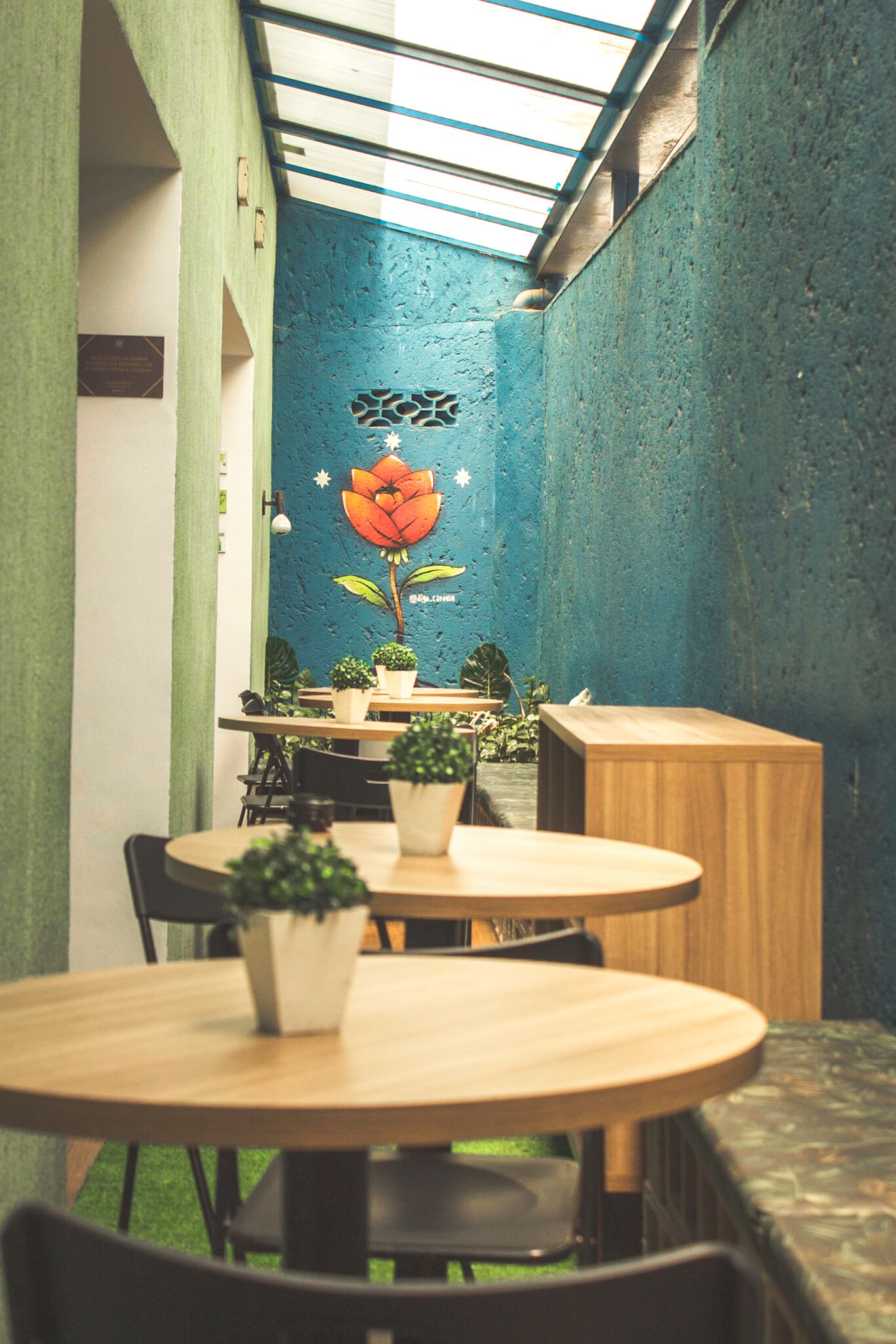 A cozy indoor dining area with round tables and chairs, potted plants, and a blue textured wall with a floral mural.