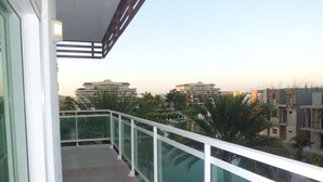 A balcony with a glass railing overlooking a residential area with multiple buildings and palm trees.