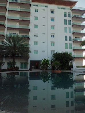 Un hotel de varios pisos con una piscina reflectante al frente.