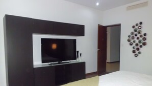 A bedroom with a bed, a TV mounted on a dark wall, a door, and a wall decoration.