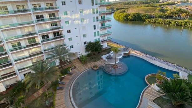 A high-rise hotel with a pool surrounded by palm trees and a view of a lake.