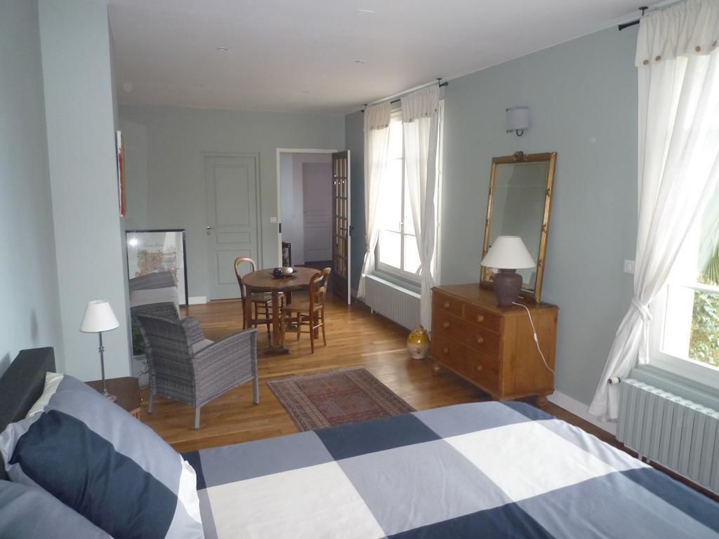 A bedroom with a bed, a dresser, a mirror, a desk with chairs, and a window with curtains.