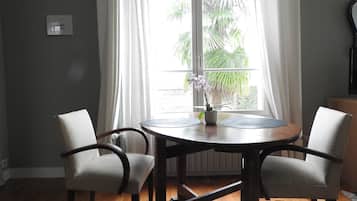 Een eetgedeelte met een ronde tafel, twee stoelen, een vaas met bloemen en een raam met gordijnen.