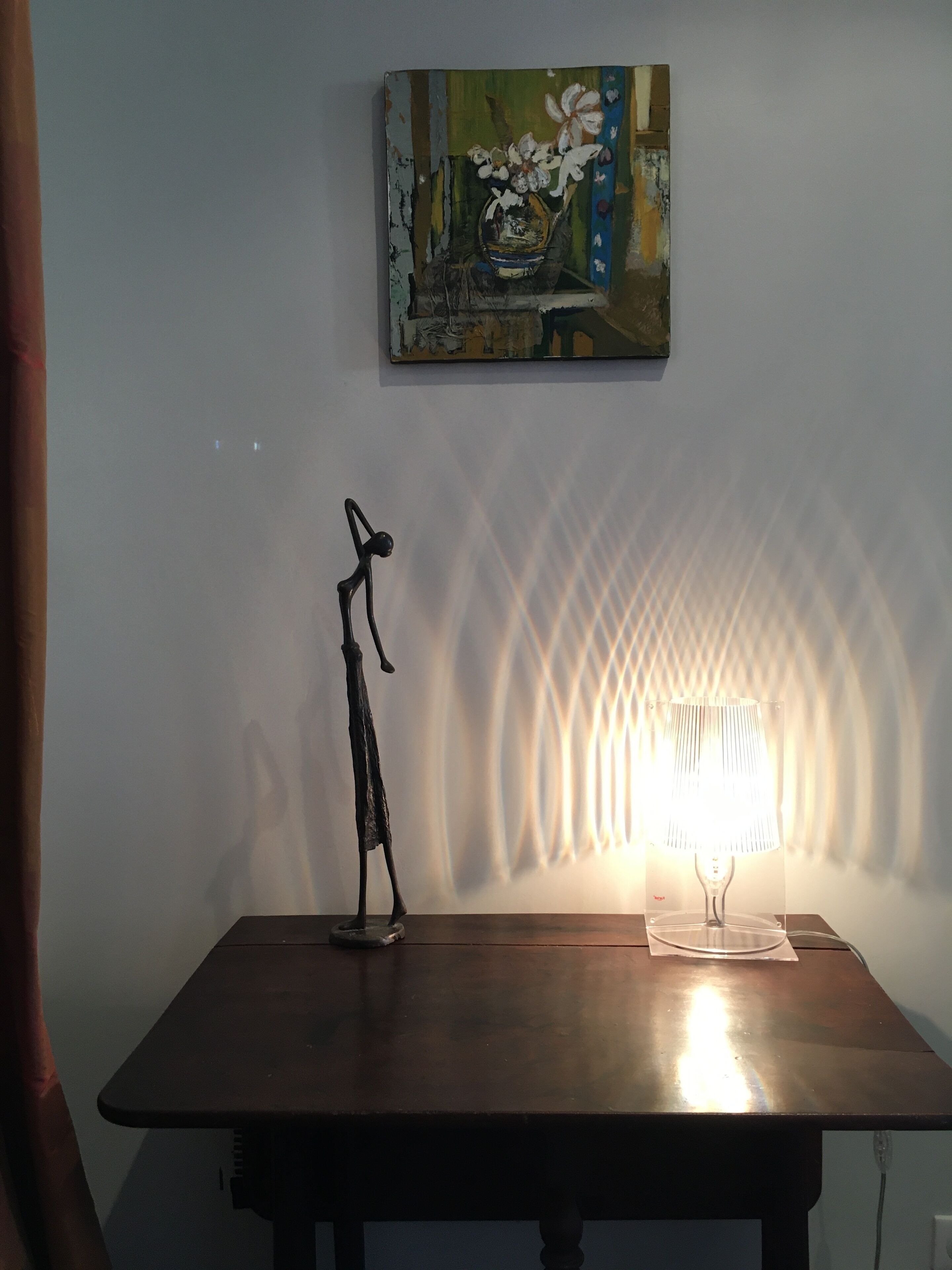 Una mesa con una escultura y una lámpara, un cuadro en la pared y un diseño decorativo en la pared.