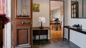 A hallway with a wooden door, a table with a lamp, and a dining area with chairs and a table. - Chambre d'hôte La Bacotterie (Bois-le-Roi)