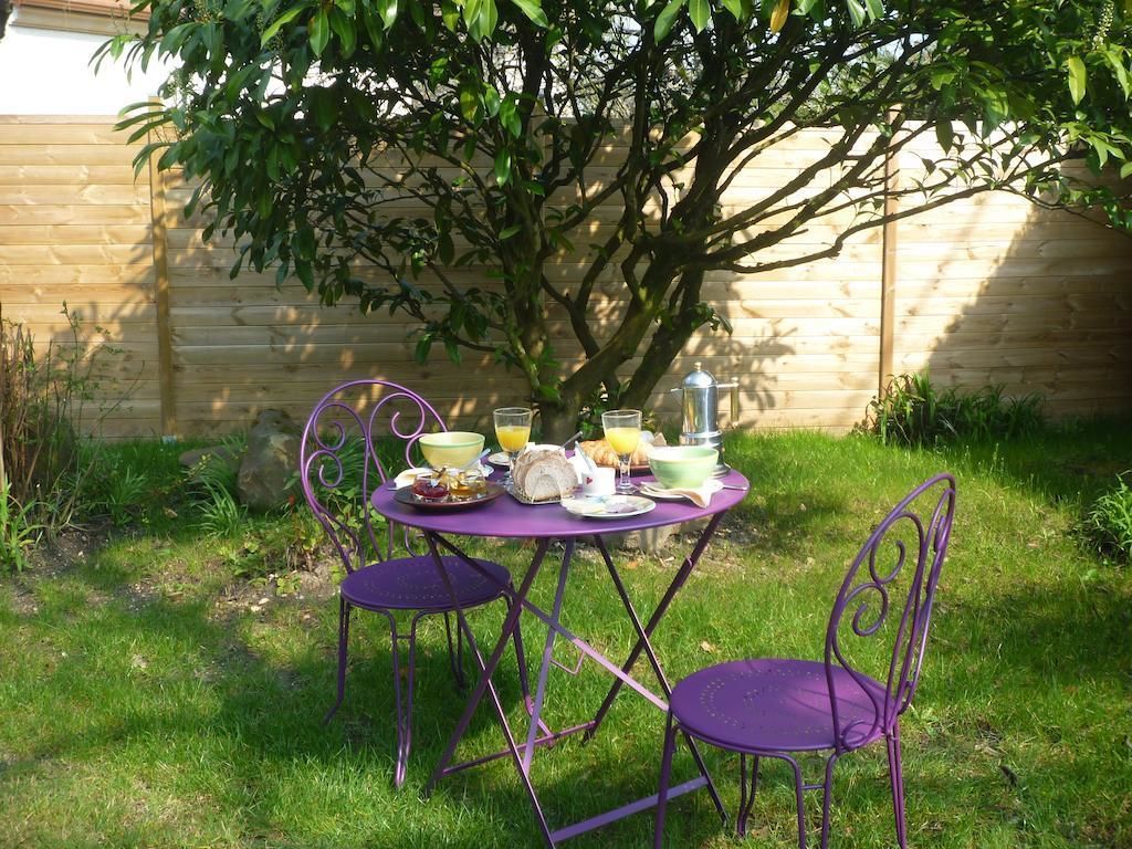 A table set outdoors with purple chairs, surrounded by greenery and a wooden fence.