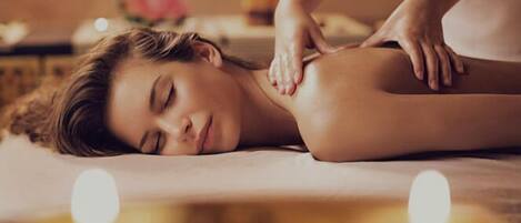 Une personne reçoit un massage sur un lit, avec des bougies en arrière-plan.