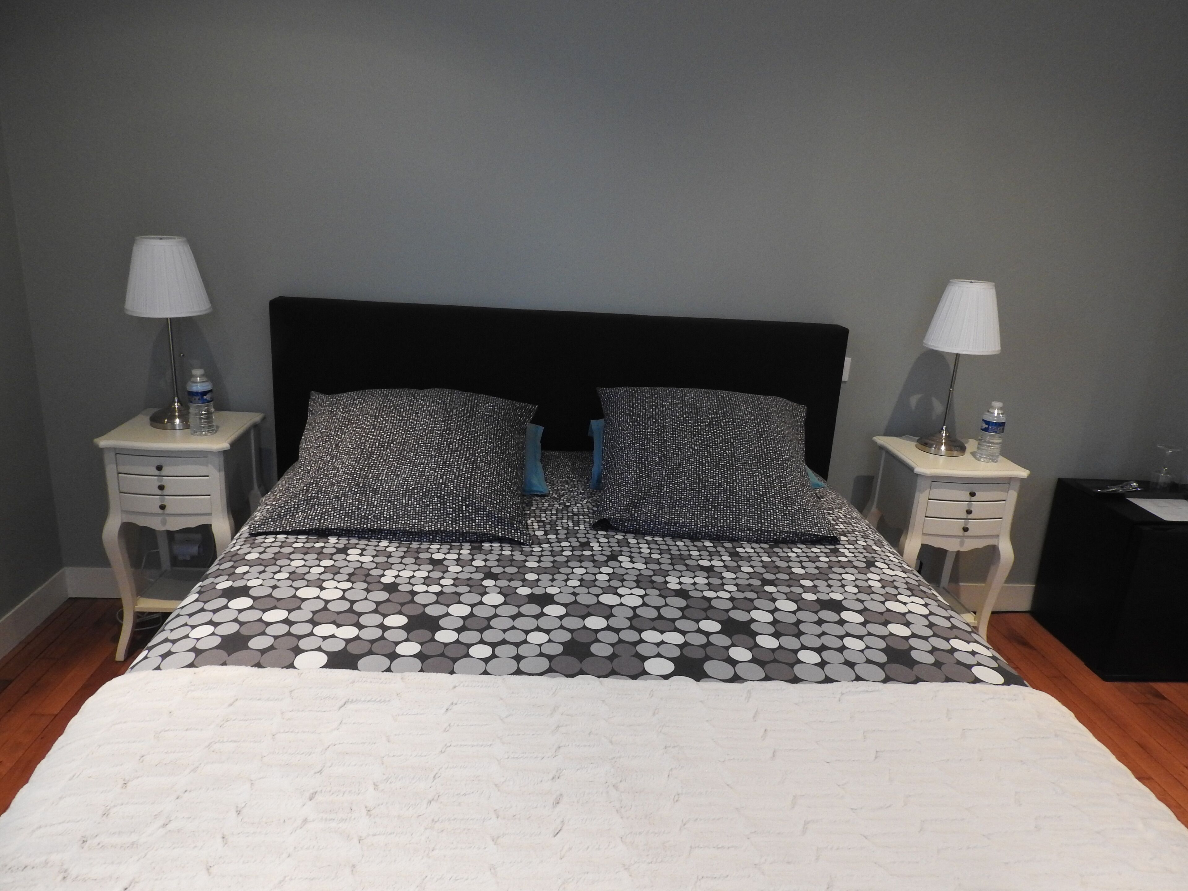 A bed with a black headboard, two white nightstands with lamps, and a patterned bedspread.