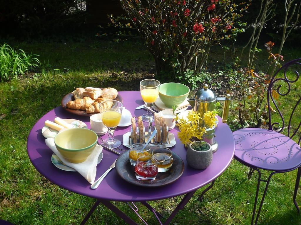 Ett runt bord dukat utomhus med ett urval av frukosträtter, inklusive bakverk, frukt och drycker.