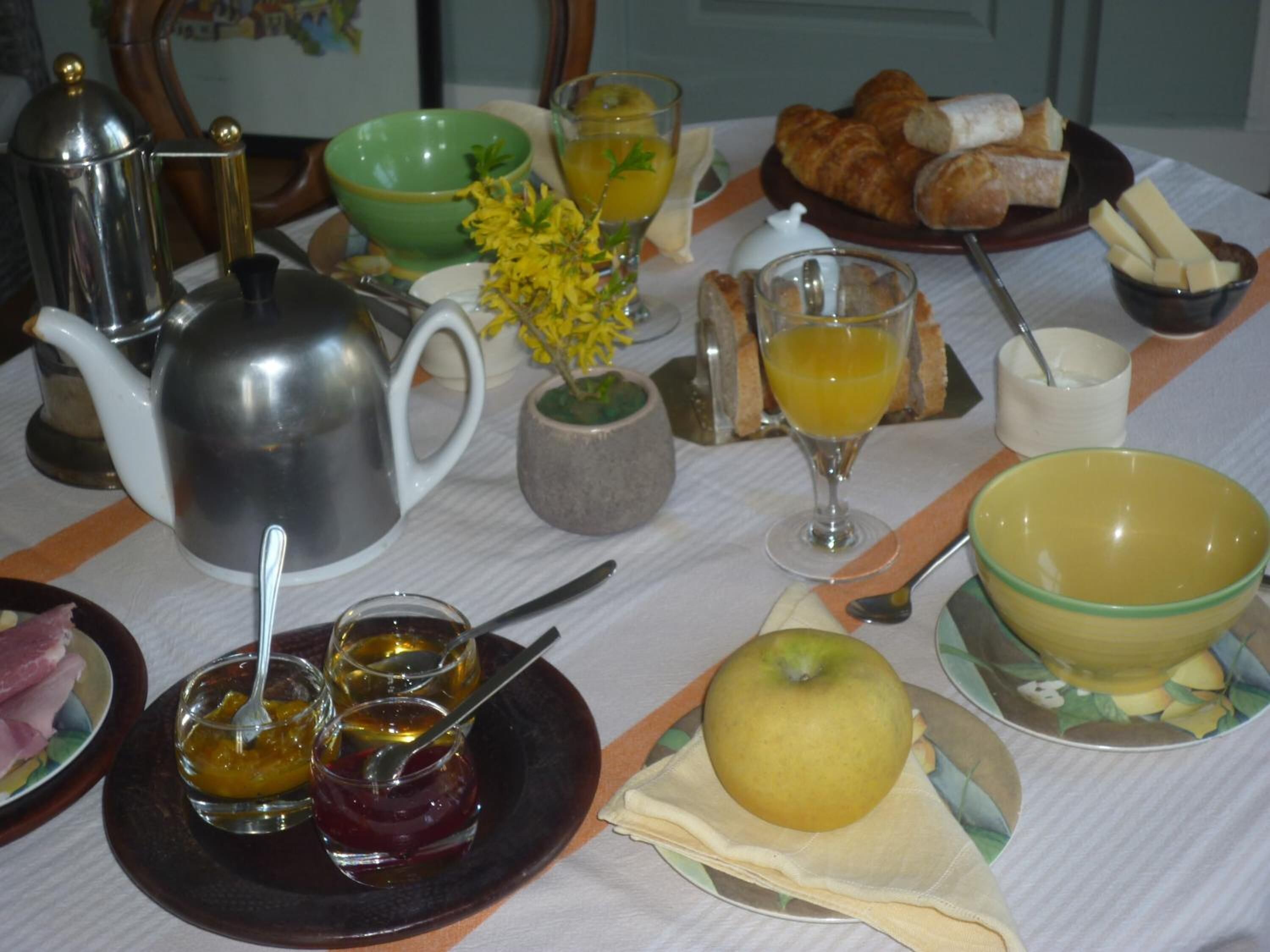 A breakfast table with various items including a teapot, cups, a bowl of fruit, and pastries.