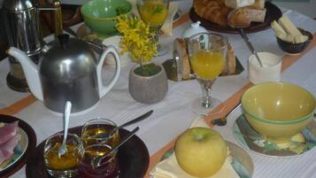 A breakfast table with various items including a teapot, cups, a bowl of fruit, and pastries.