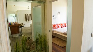 A modern hotel room with a glass partition, a bed with a red and white patterned bedspread, and a small indoor garden with plants and rocks. - Villas Agua Dulce - Villa Eden (Sosúa)