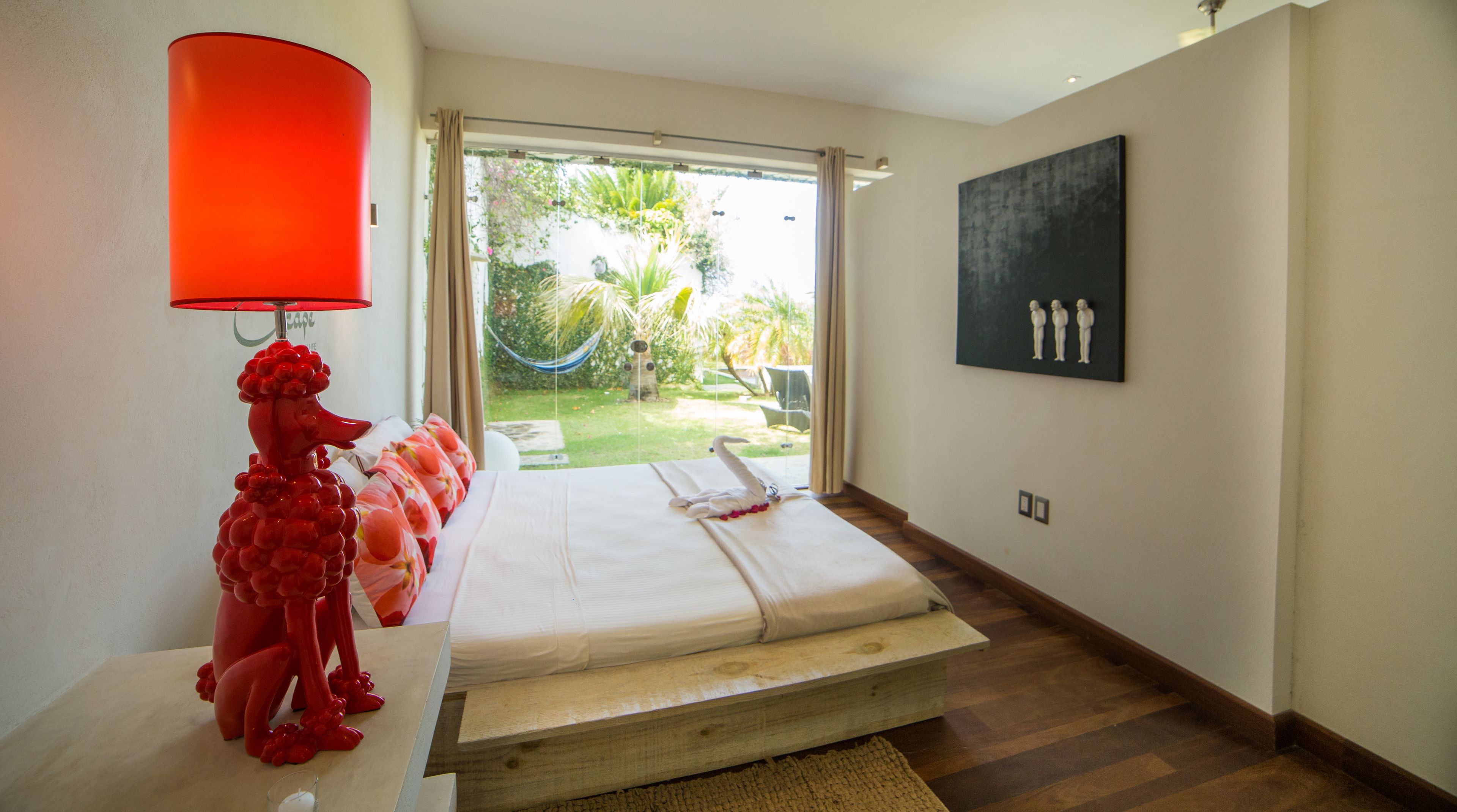 A bedroom with a bed, a red lamp, a painting, and a view of the garden.