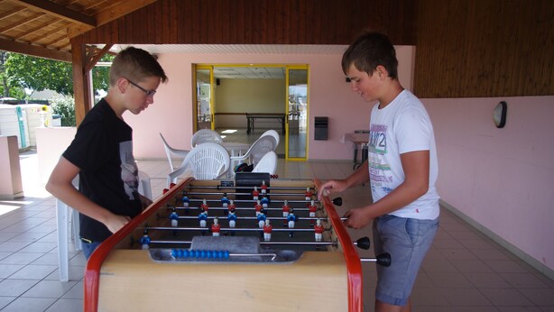 Two individuals playing foosball in an indoor setting with a wooden ceiling and tiled floor. - Camping La Corniche (Plozevet)