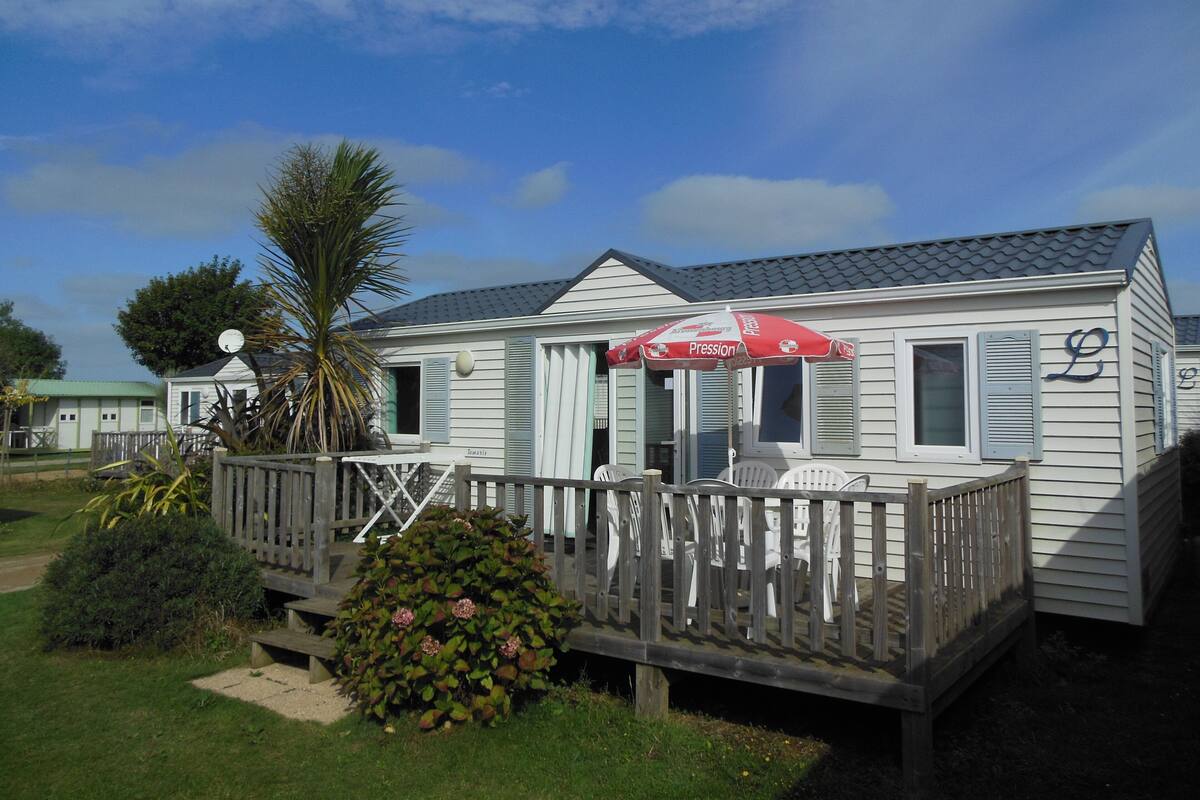 A white mobile home with a porch, a red umbrella, and a wooden deck.
