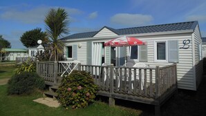 A white mobile home with a porch, a red umbrella, and a wooden deck. - Camping La Corniche (Plozevet)