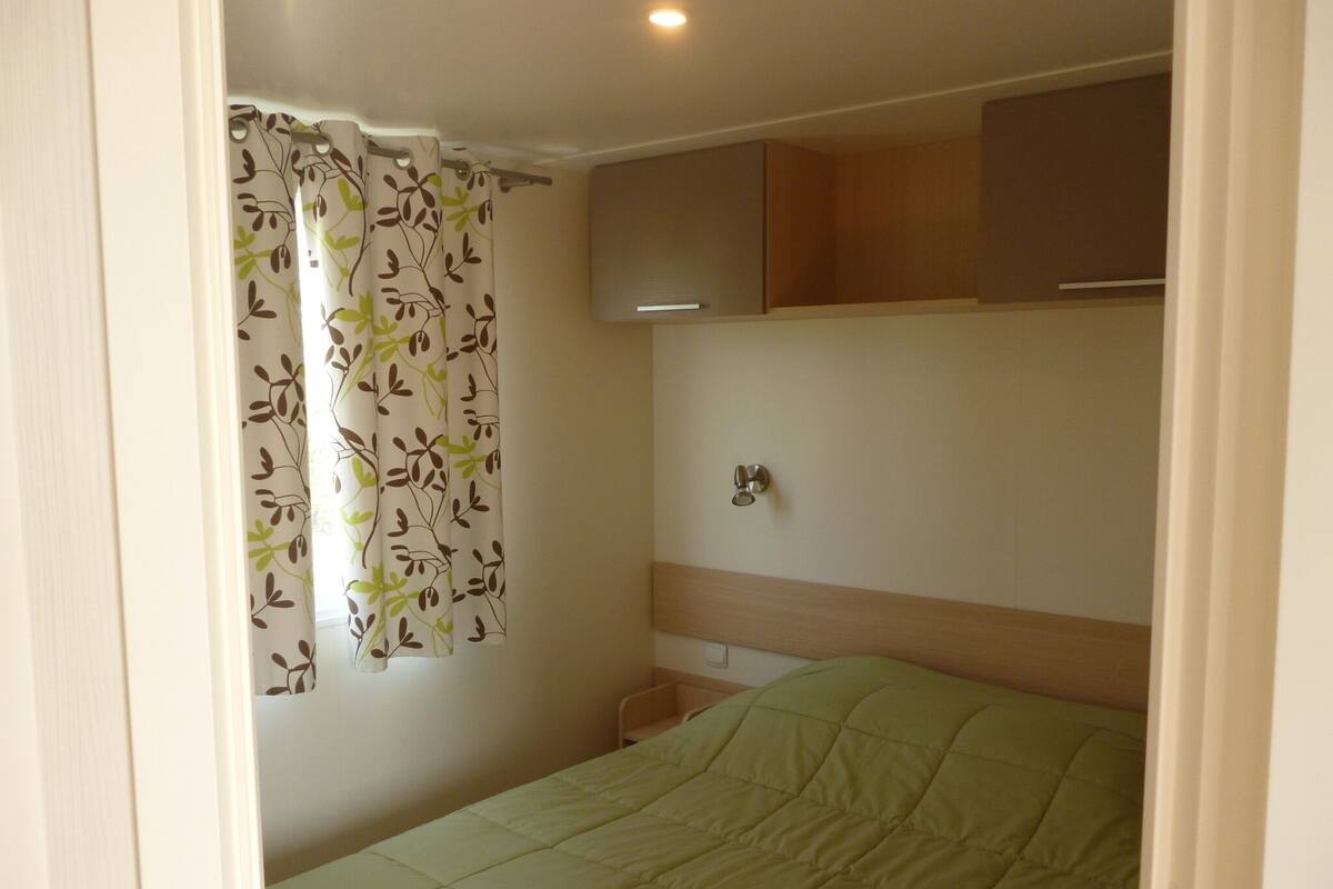 A bedroom with a bed, a wall-mounted cabinet, and a window with a curtain.