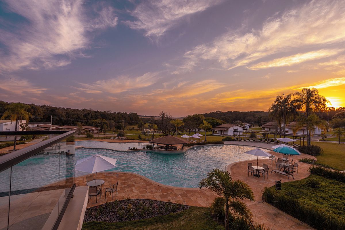 A swimming pool with a sunken area, surrounded by outdoor seating and umbrellas, with a view of a residential area in the background.