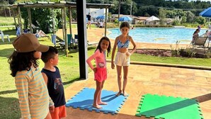 Un groupe d’enfants se tient sur des tapis de mousse emboîtables à l’extérieur, avec une piscine et un espace abrité en arrière-plan.