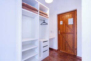 Ein begehbarer Kleiderschrank mit mehreren Regalen und Kleiderstangen, eine Holztür mit einem Schild und ein gefliester Boden.