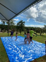 Um grupo de pessoas brincando em um tapete azul coberto de espuma sob uma tenda.