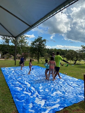 A group of people playing on a blue foam-covered mat under a tent.