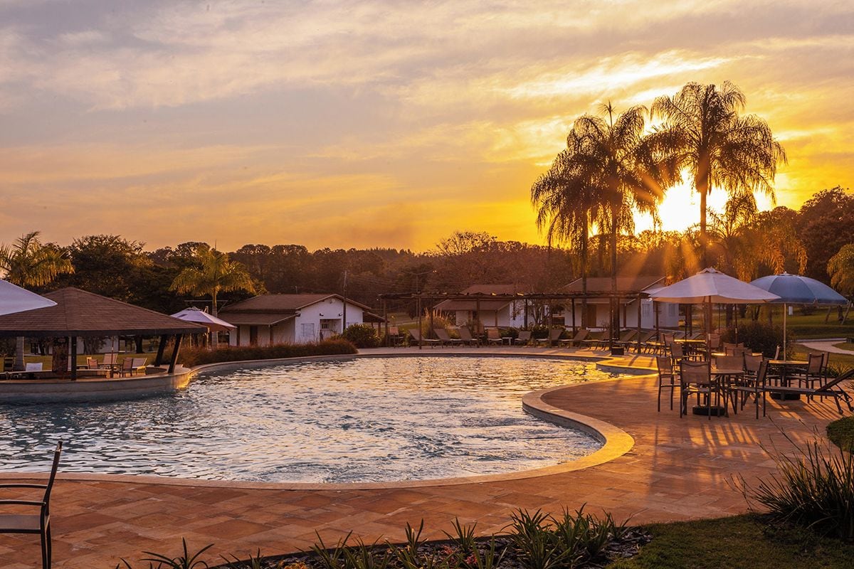 Una piscina con sillas de descanso y sombrillas, rodeada de edificios y palmeras.