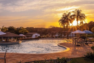 Una piscina con sillas de descanso y sombrillas, rodeada de edificios y palmeras.