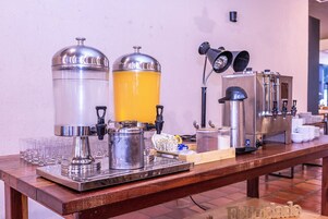 Una estación de barista con una máquina de café, espumador de leche y una jarra de jugo de naranja.