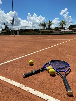 A tennis court with a net, two tennis rackets, and three tennis balls.