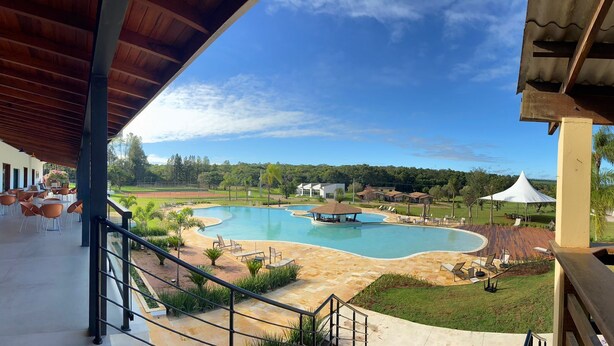 A swimming pool with a curved design, surrounded by lounge chairs and a covered seating area. - Vale das Águas Fazenda Resort (Aguas de Santa Barbara)