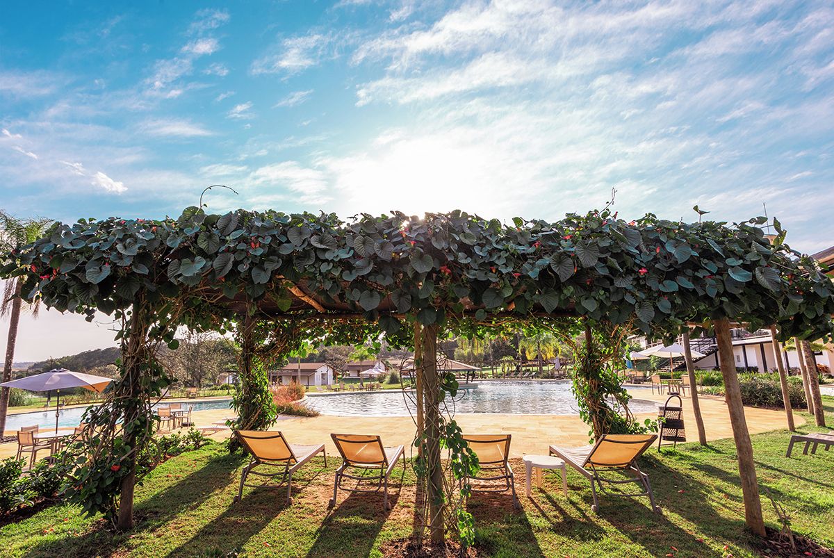 A covered outdoor seating area with chairs and a pool in the background.