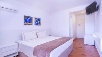 A bedroom with a bed, a nightstand, a TV mounted on the wall, and two paintings of parrots.