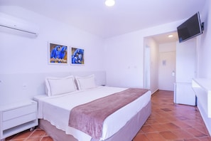 A bedroom with a bed, a nightstand, a TV mounted on the wall, and two paintings of parrots.
