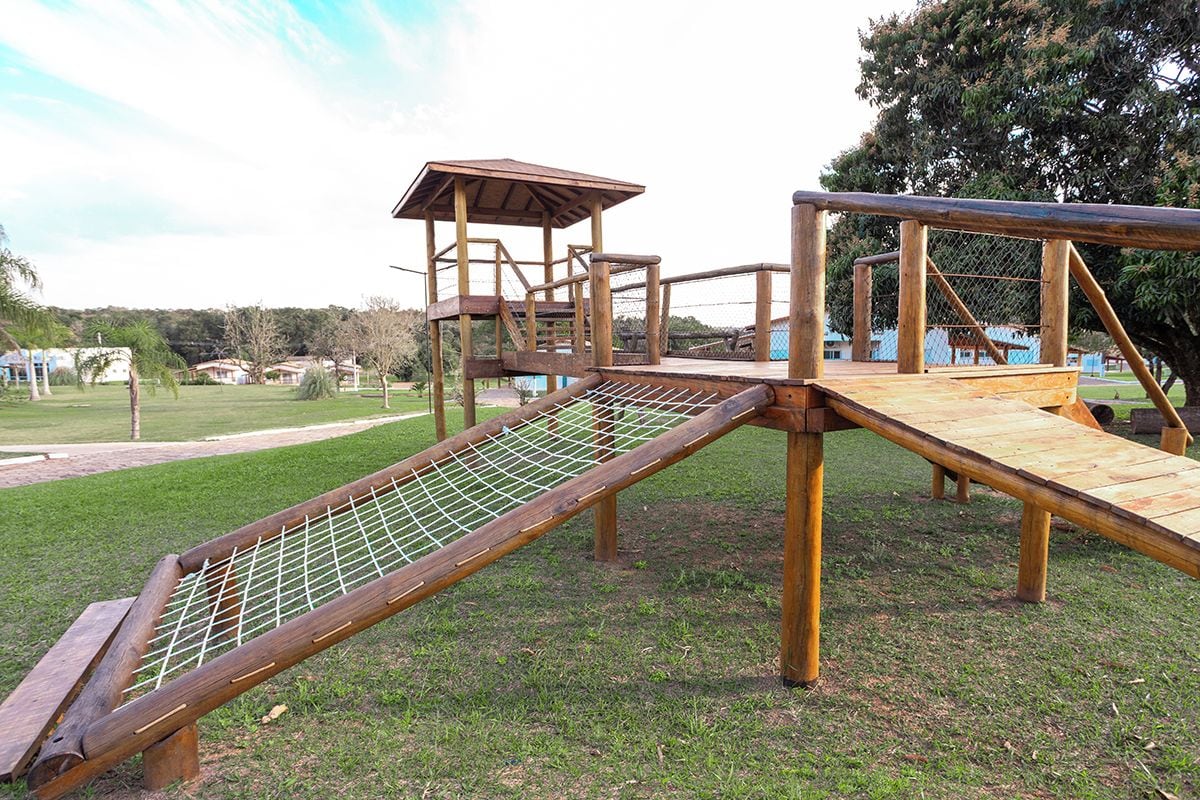 Ein Spielplatz mit einer hölzernen Kletterkonstruktion, einer Rutsche und einem eingezäunten Bereich.
