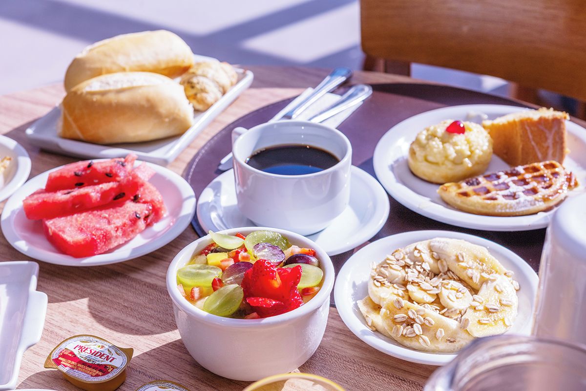 A table with various food items including pastries, a fruit bowl, and a cup of coffee.