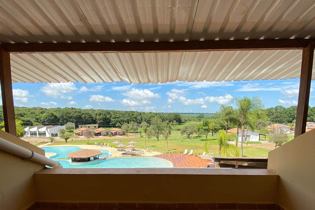Un balcon avec deux fauteuils en osier, une vue sur une piscine et un paysage verdoyant avec des arbres et des bâtiments.