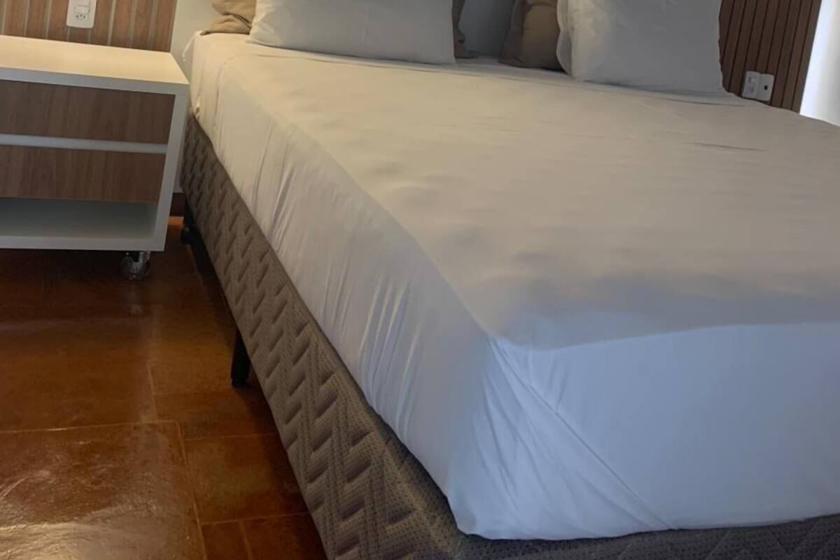 Un lit bien fait, avec une tête de lit, une table de chevet et un luminaire suspendu.