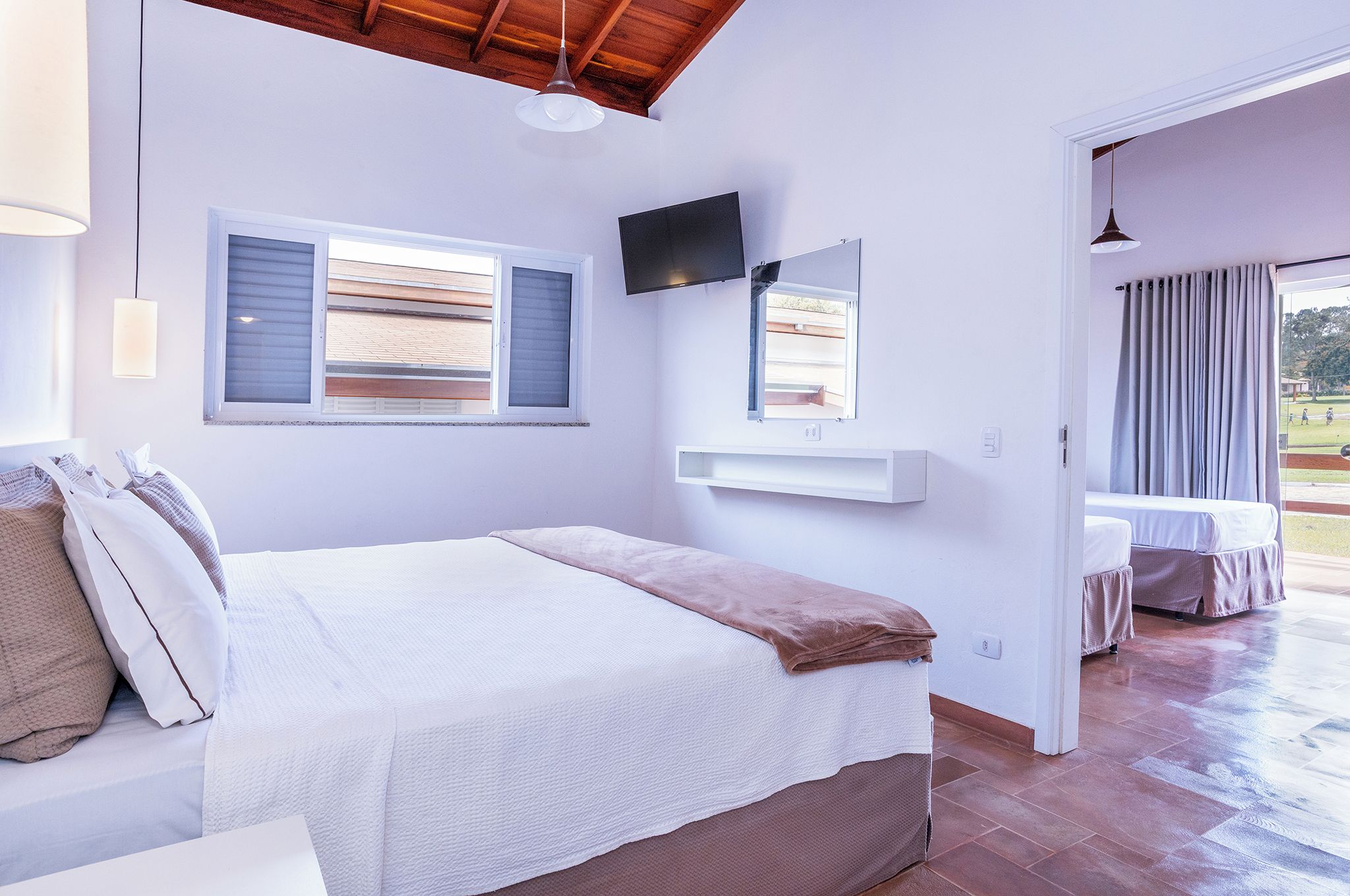 A bedroom with a bed, a TV mounted on the wall, and a window with blinds.