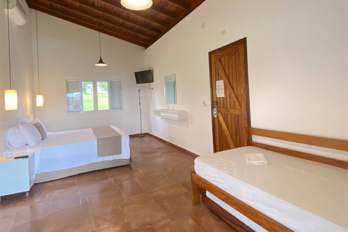 Une pièce spacieuse avec un plafond en bois, un lit, un banc, un téléviseur et une porte.