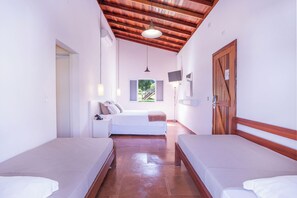 A room with two beds, a wooden ceiling, a window with shutters, and a door.