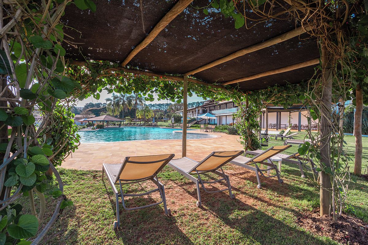 A poolside area with lounge chairs, a covered patio, and a view of buildings in the background.